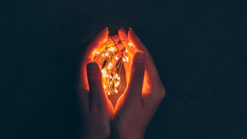 Two open hands cradling a small warm light in the dark, the difficult practice of turning ordinary kindness towards oneself