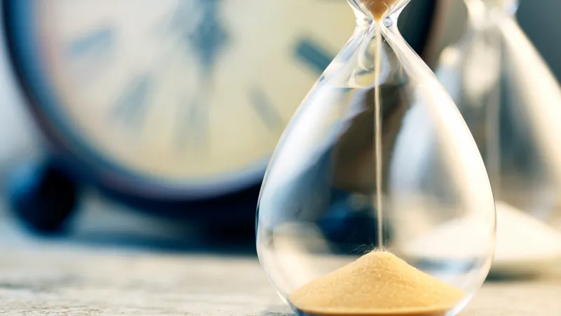 An hourglass running quietly beside a pale clock face, a whole lifetime measured against the handful of hours anybody was genuinely present for