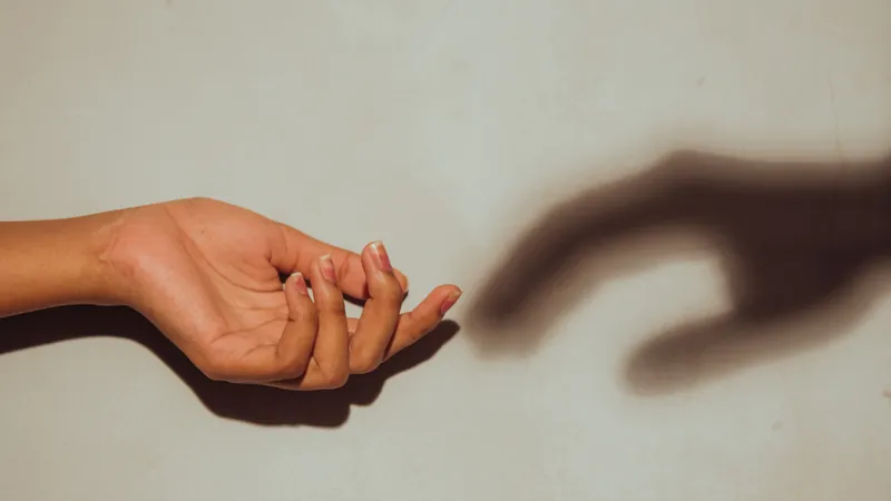 A hand and its own shadow reaching towards each other across pale empty ground, a boundary moved back so gradually that nobody noticed it going
