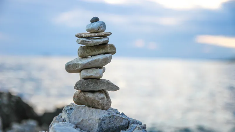 A tall cairn of smooth stones standing quietly against an open sea and a pale sky, silence that is full rather than absent
