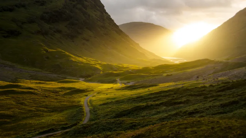 Sunlight breaking over a wide green valley with a single path winding through it, seeing a thing as it actually is rather than as we wish it were