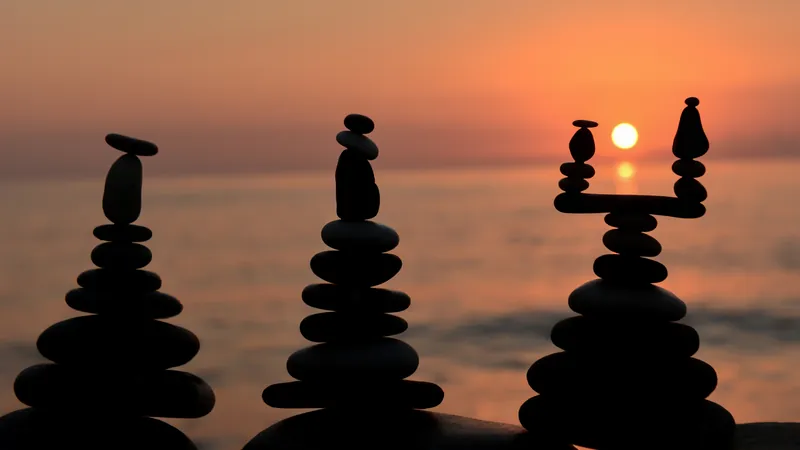 Balanced stone cairns silhouetted against a burning sunset over still open water, the directions a life can grow in that nothing ever measures