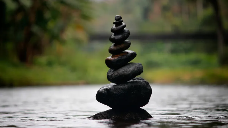 A cairn of dark stones balanced on the mirror-still surface of a river, the longing to be seen exactly as one actually is